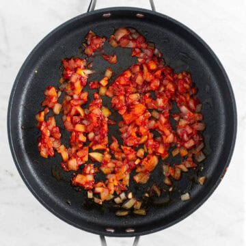 Sautéed onion and garlic with tomato paste, salt, pepper, and red pepper flakes in a skillet.