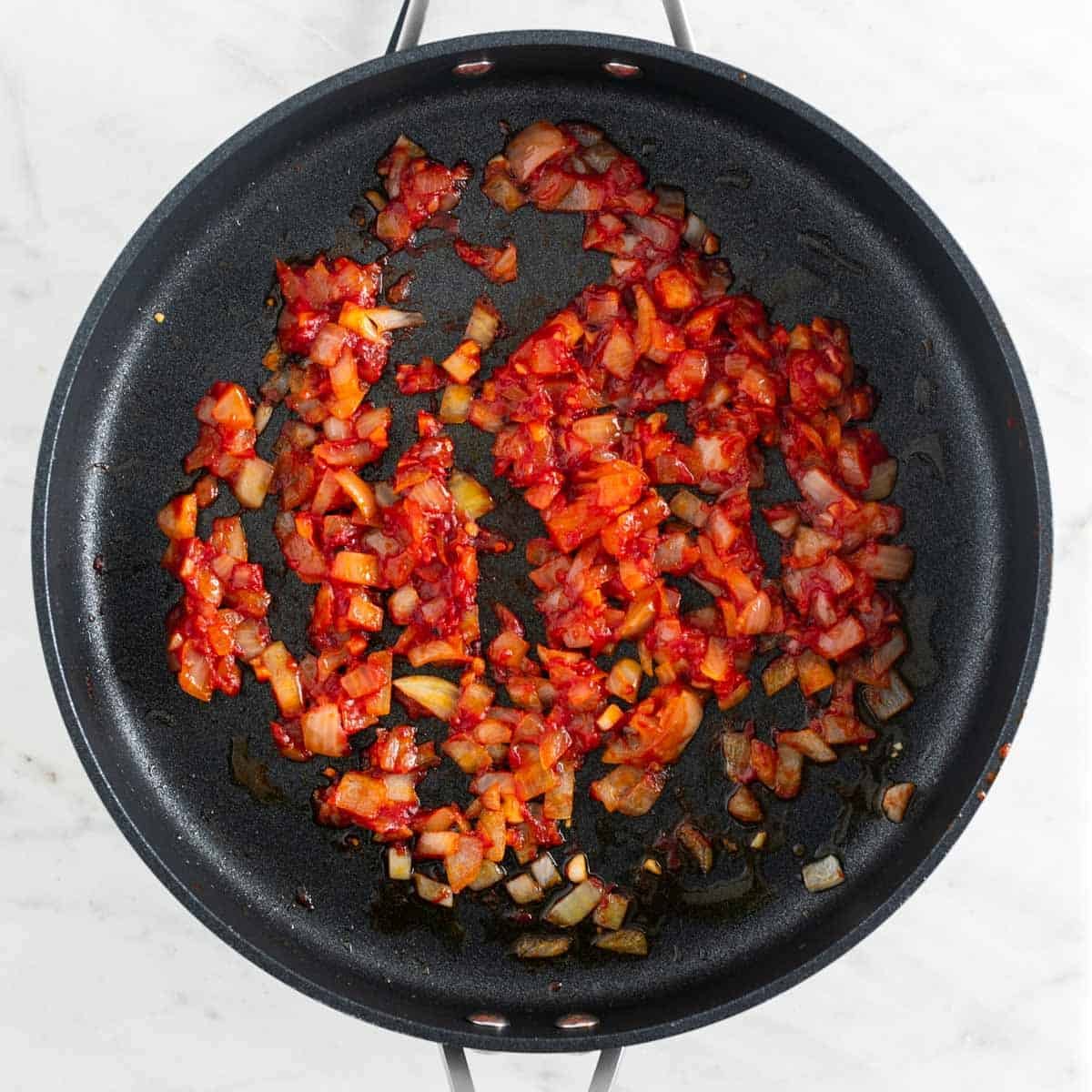 Sautéed onion and garlic with tomato paste, salt, pepper, and red pepper flakes in a skillet.