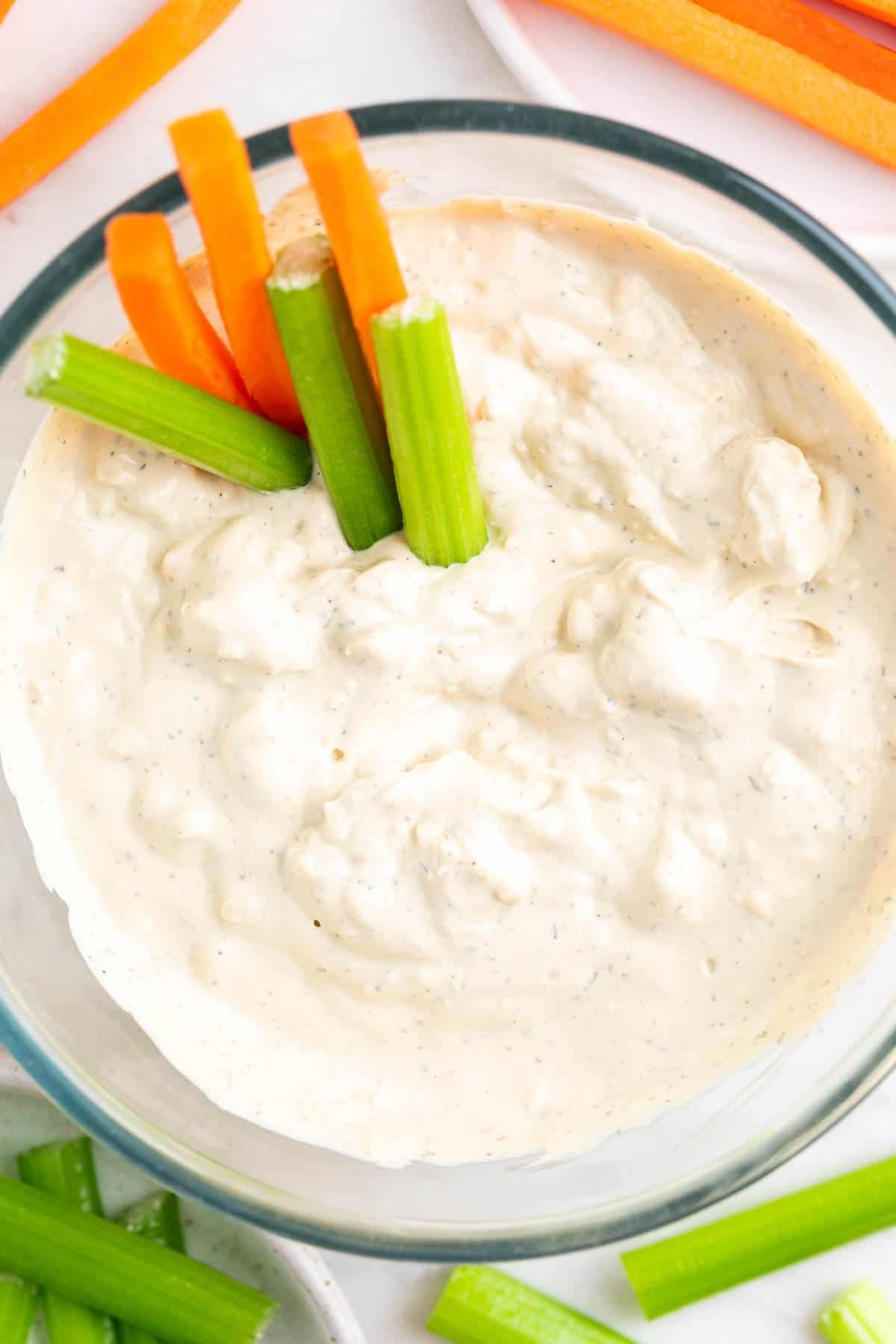 Bowl with vegan blue cheese dressing, with celery and carrot sticks inside and around the bowl.