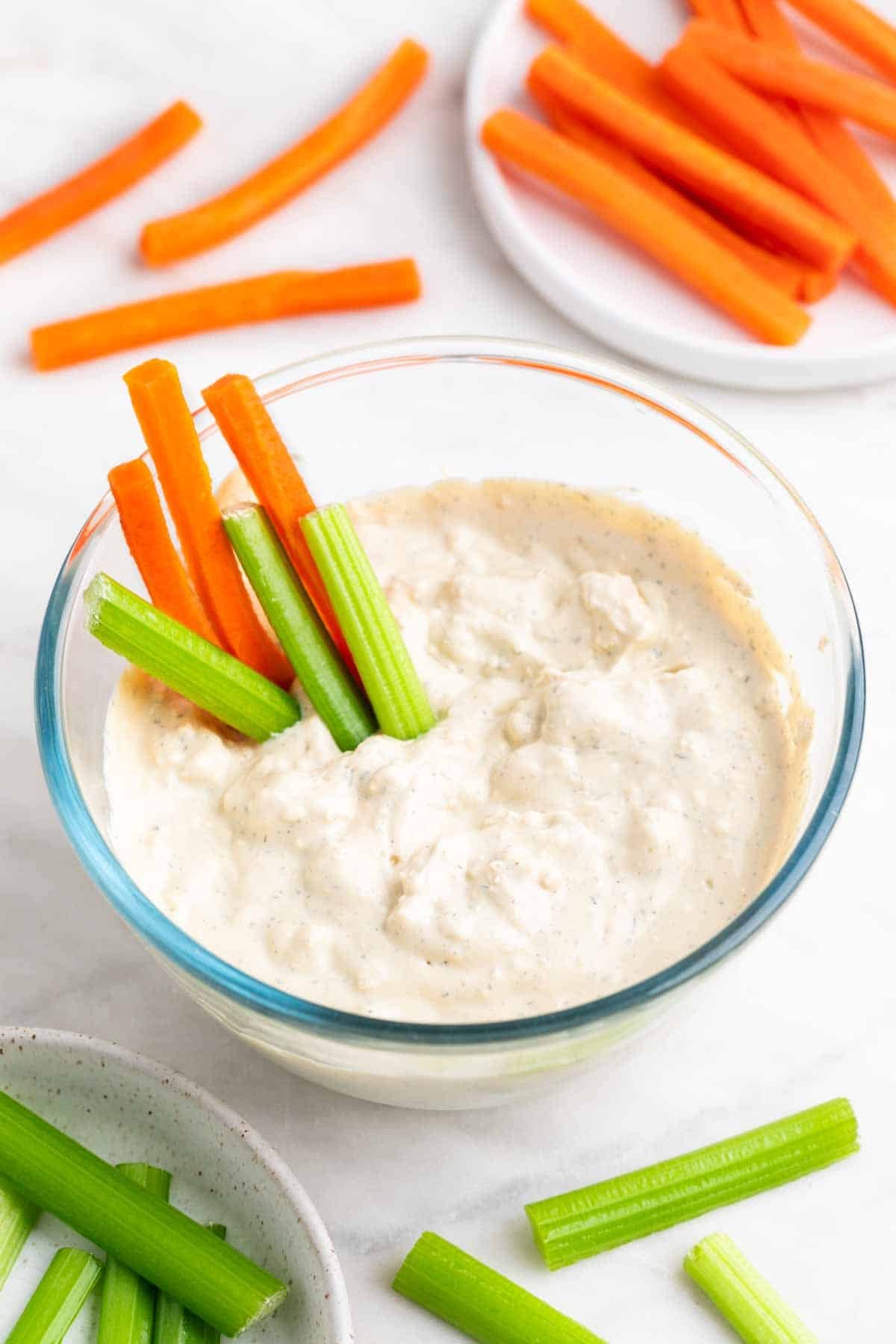 Bowl with vegan blue cheese dressing, surrounded by celery and carrot sticks.