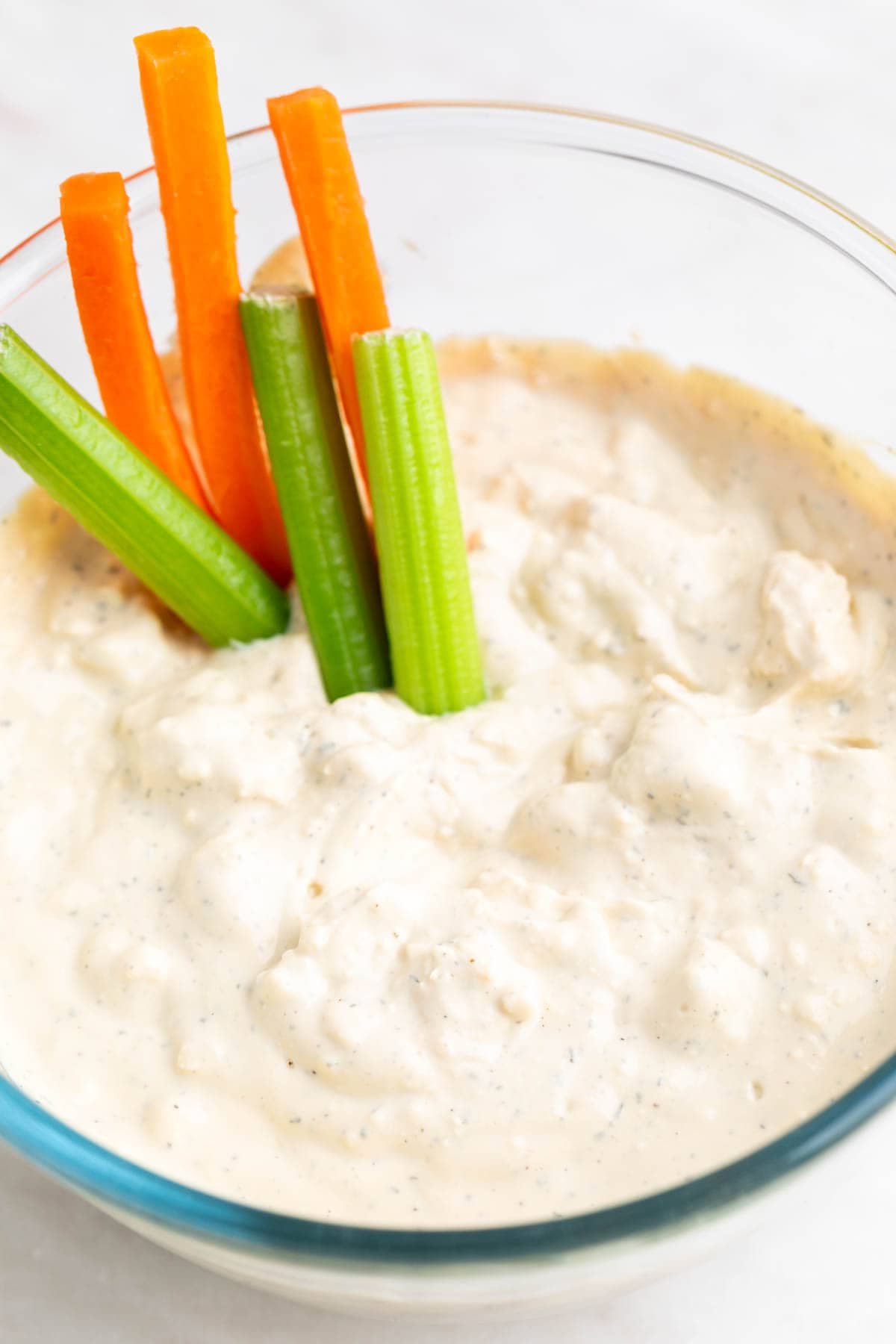 Bowl with vegan blue cheese dressing, with celery and carrot sticks inside.