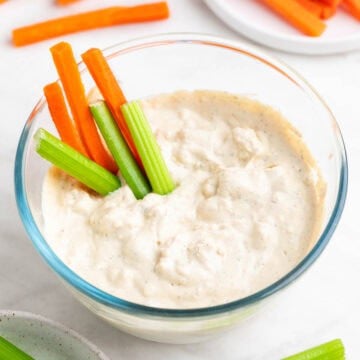 Bowl with vegan blue cheese dressing, with celery and carrot sticks inside.