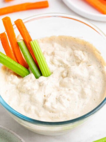 Bowl with vegan blue cheese dressing, with celery and carrot sticks inside.