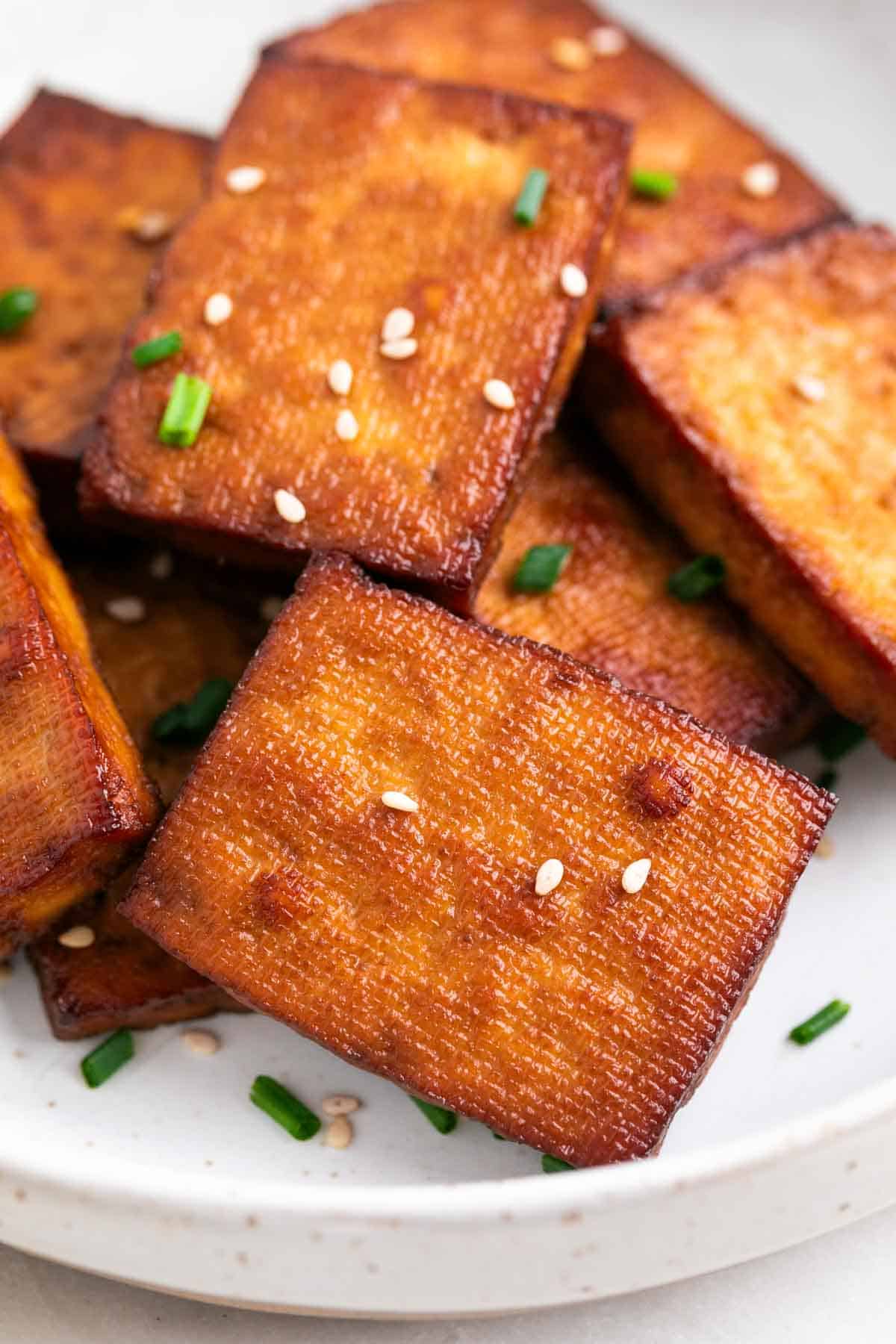 Smoked tofu on a plate, garnished with chives and sesame seeds.