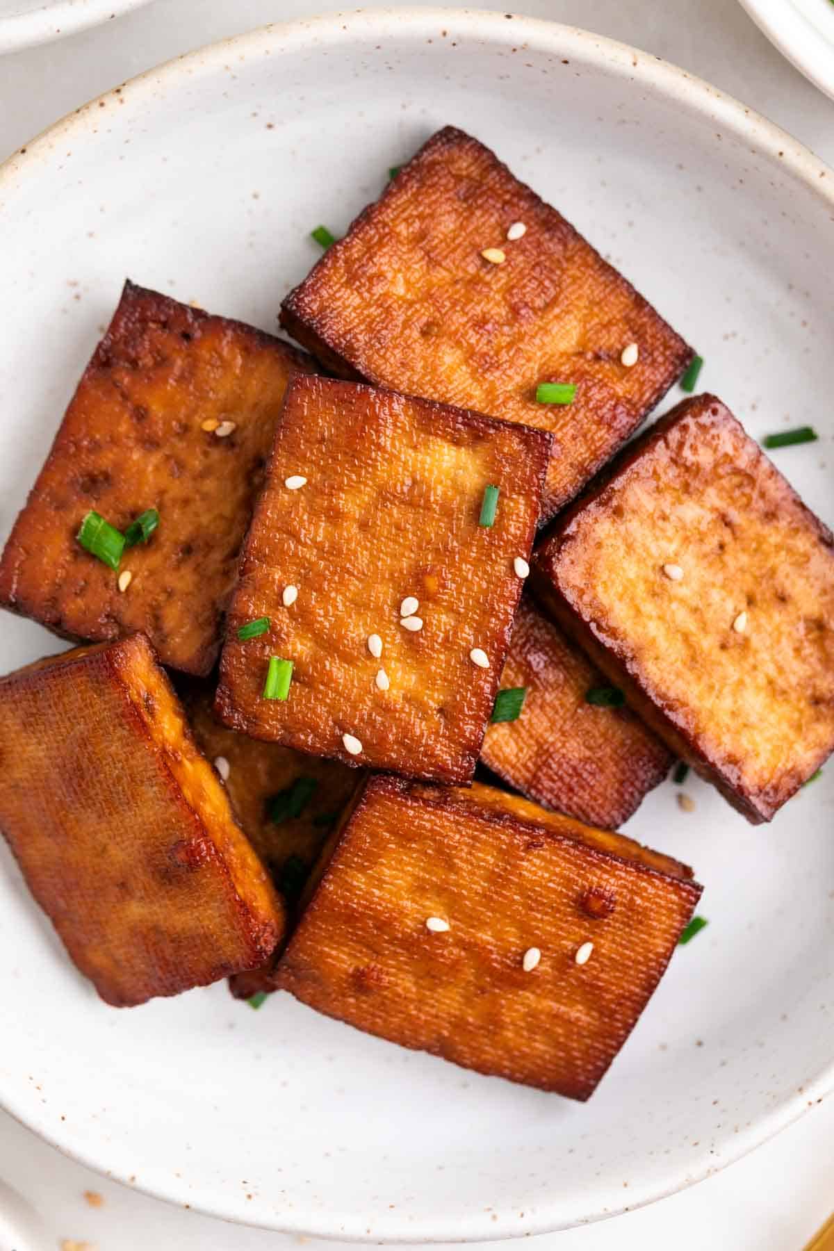 Smoked tofu served on a plate, topped with chives and sesame seeds.