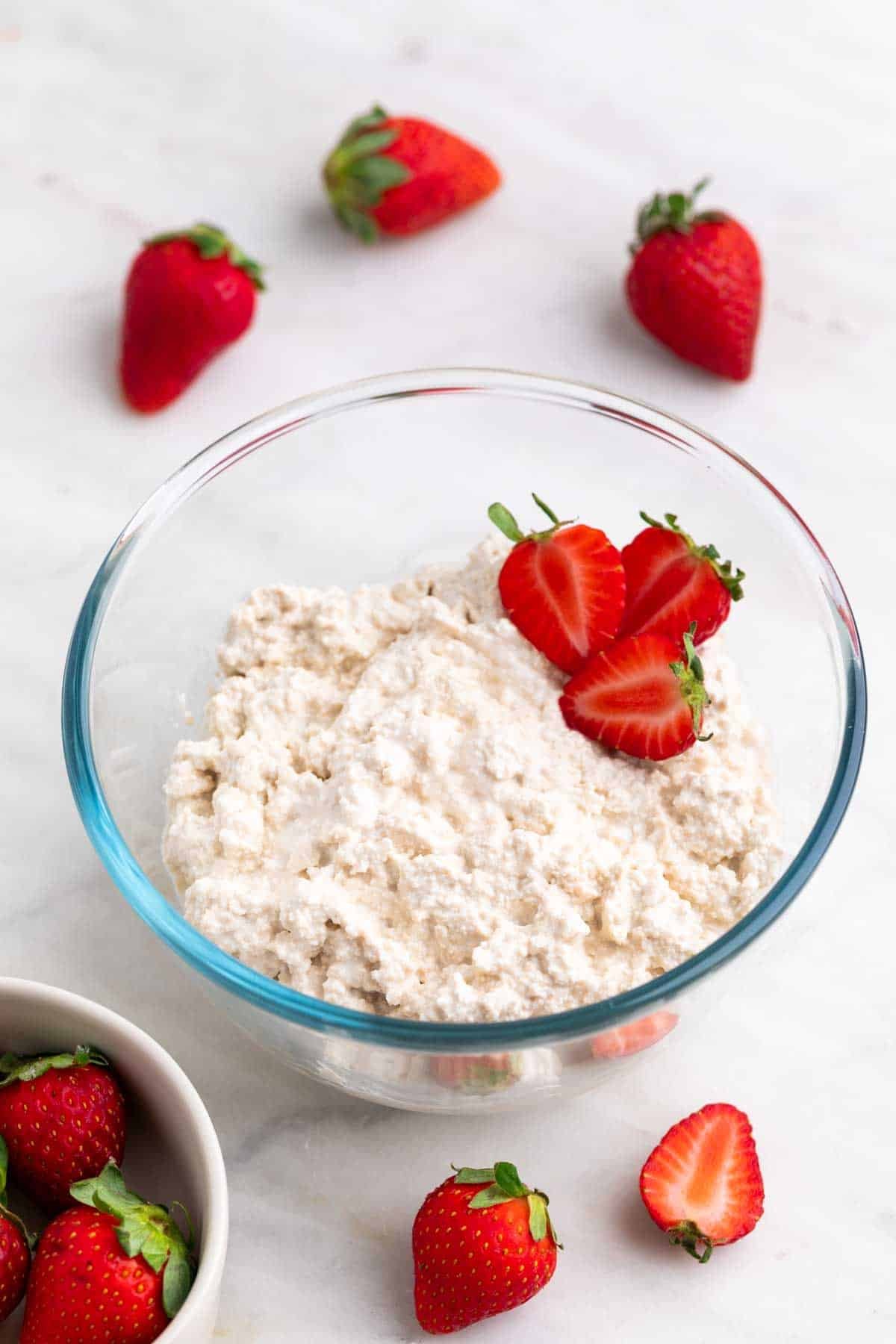 Vegan cottage cheese in a bowl with strawberries placed inside and around it.