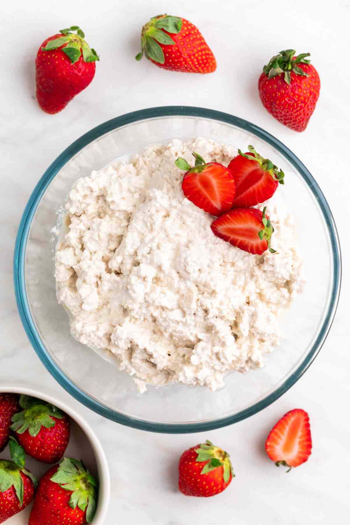 Vegan cottage cheese in a bowl with strawberries inside and around it.