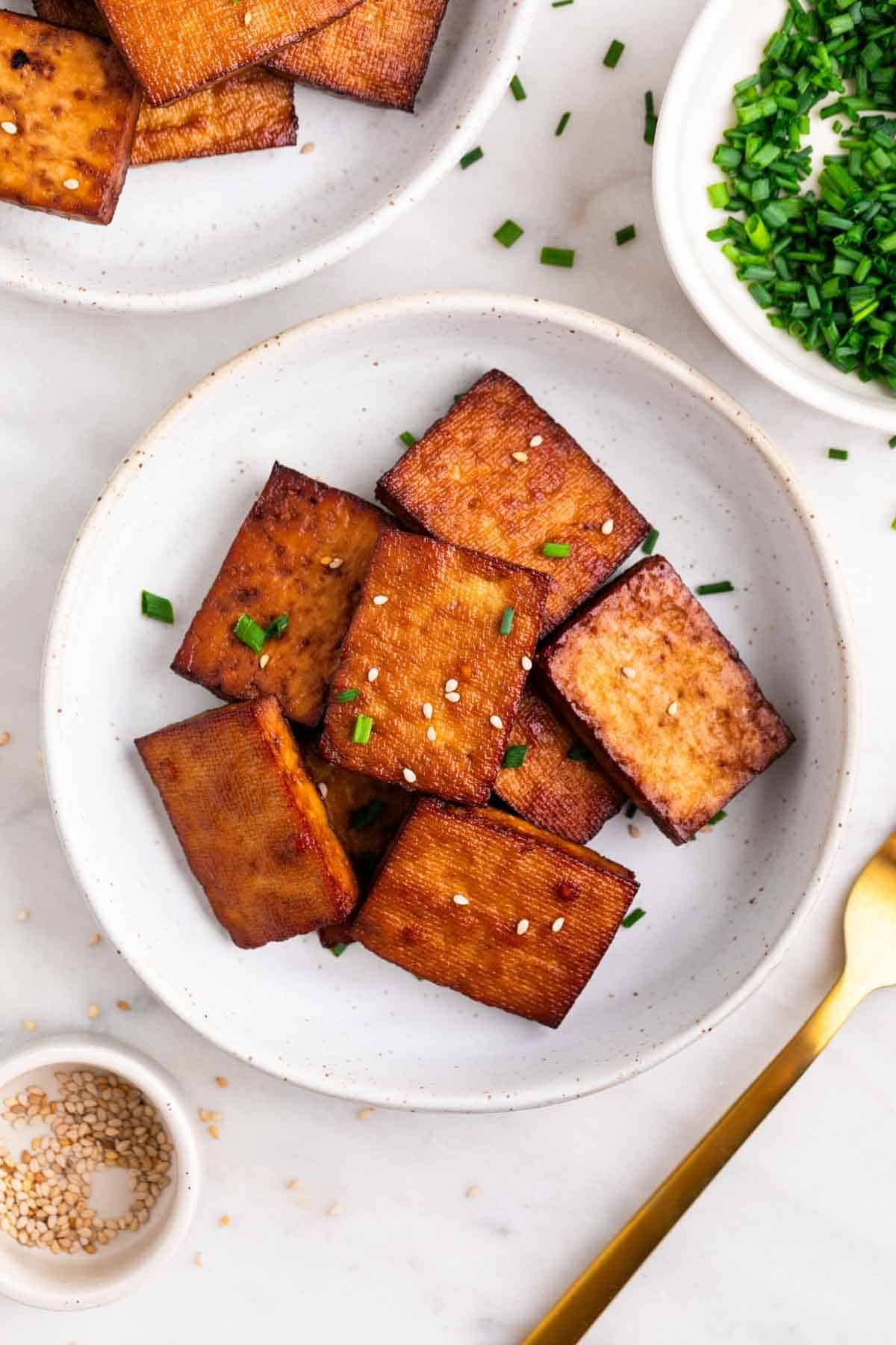 Smoked tofu garnished with chives and sesame seeds, with extra around and a fork.