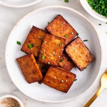 Smoked tofu garnished with chives and sesame seeds, with extra around and a fork.
