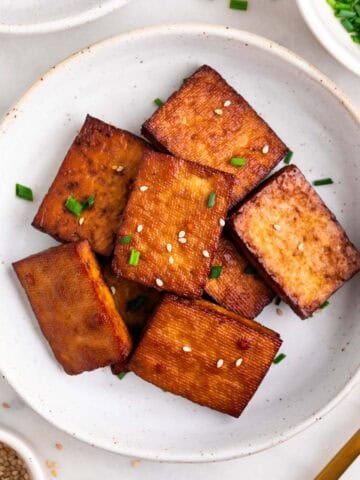 Smoked tofu garnished with chives and sesame seeds, with extra around and a fork.