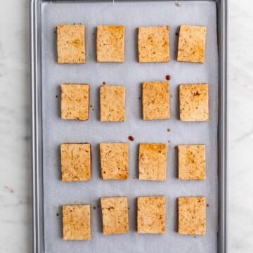 Tofu slices on a lined baking sheet.
