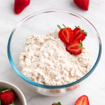 Vegan cottage cheese in a bowl with strawberries placed inside and around it.