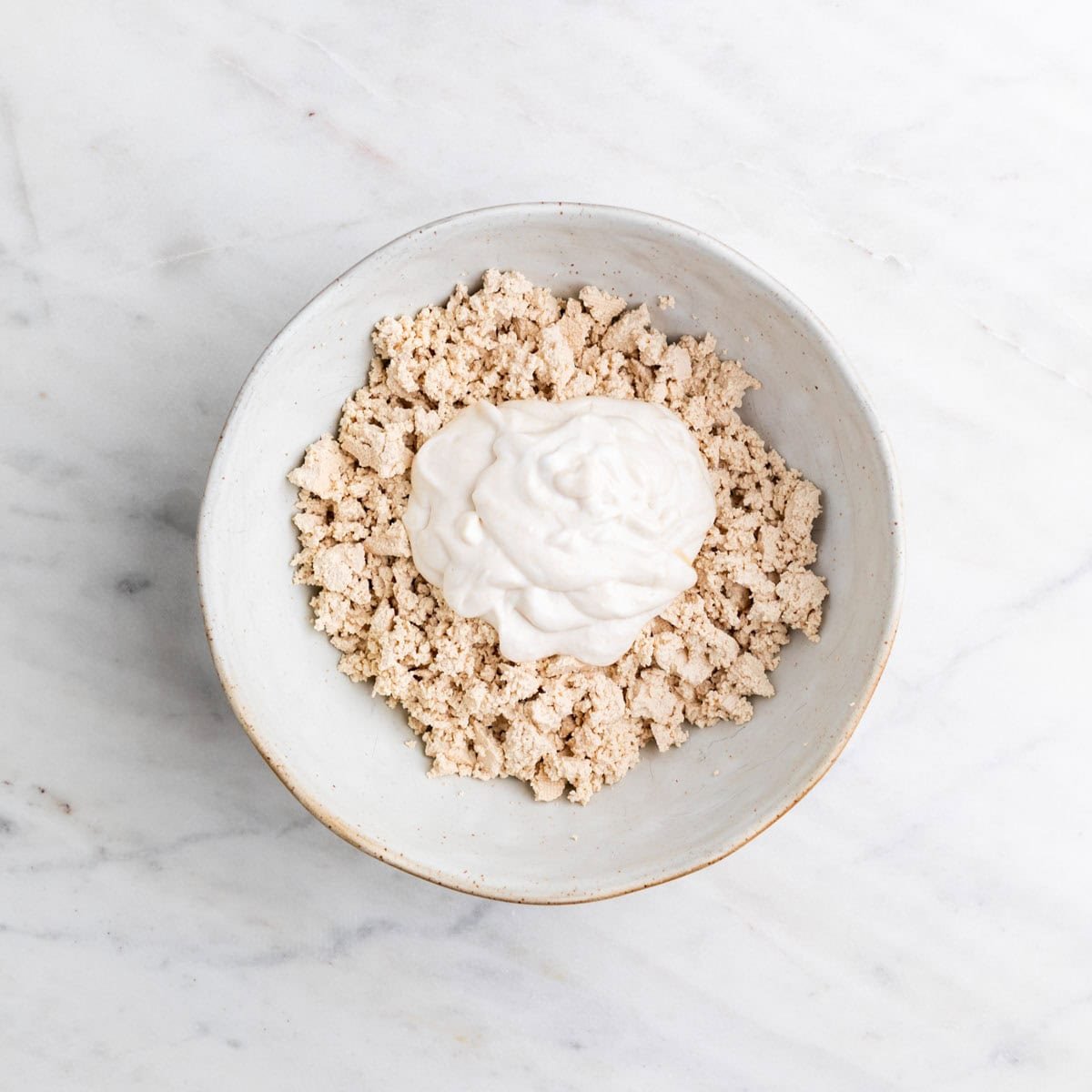 Crumbled tofu in a large bowl with the mixture of other ingredients on top.