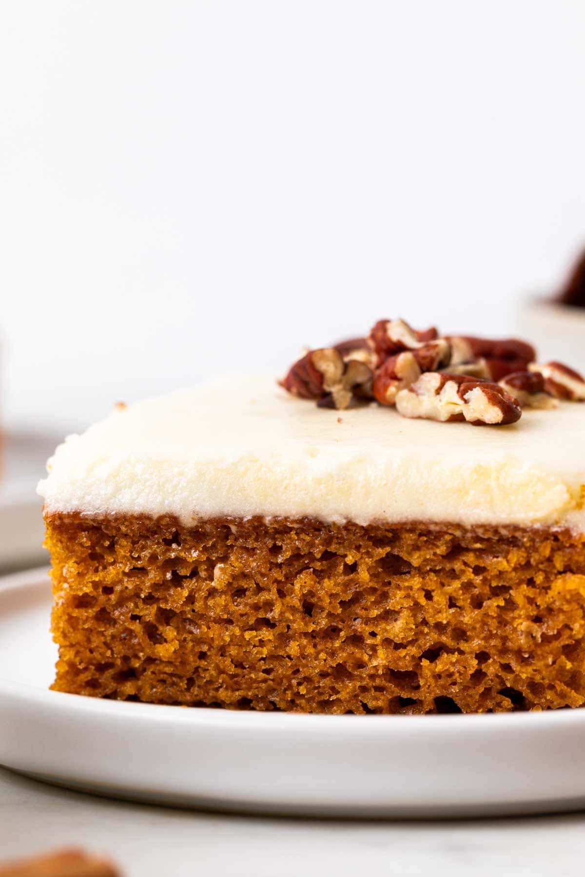 Slice of vegan pumpkin cake with vegan cream cheese frosting on a plate.