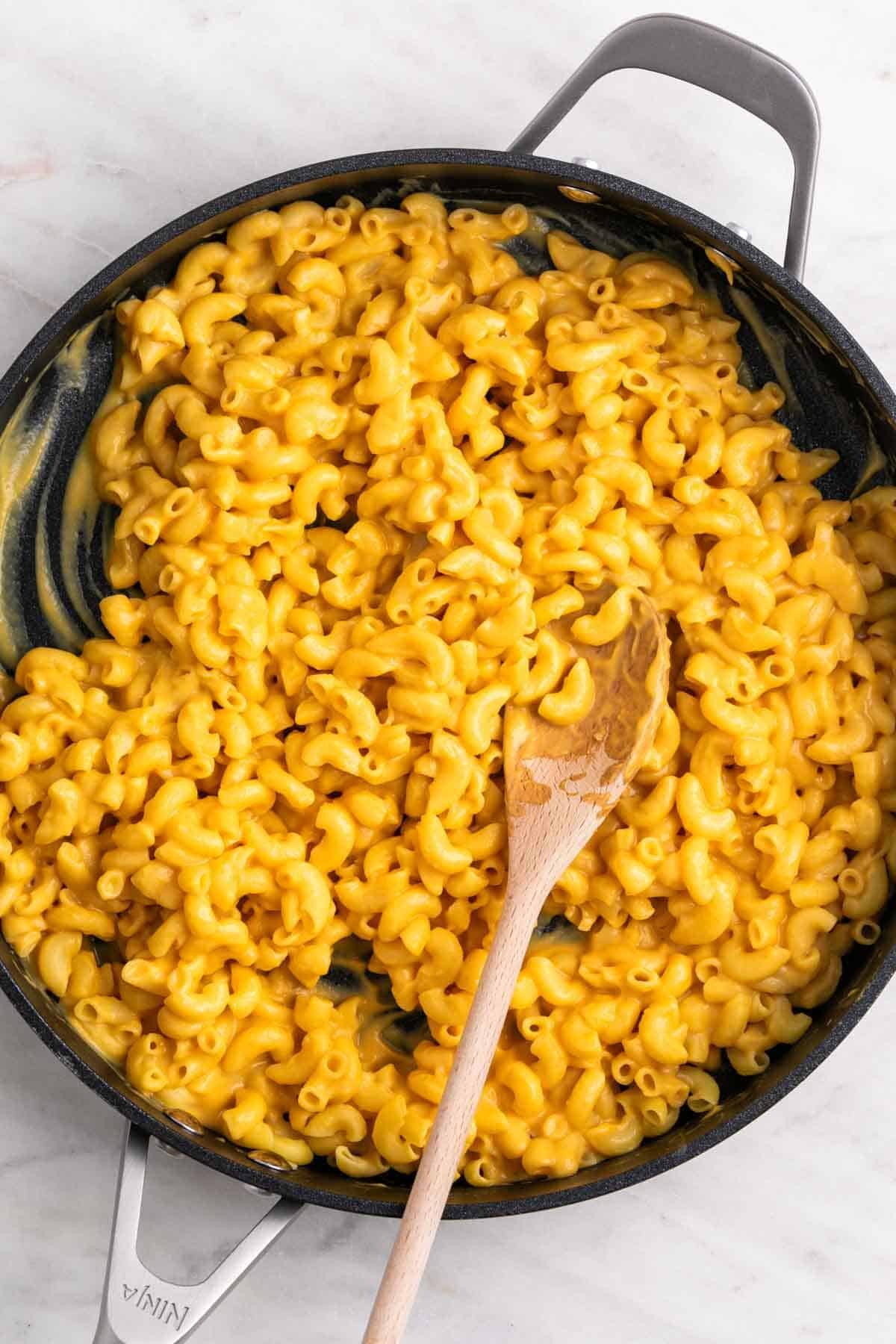 Vegan butternut squash mac and cheese in a skillet with a wooden spoon.