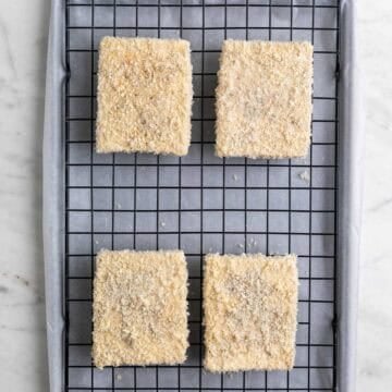 Breaded tofu pieces on a wire rack on a lined baking sheet before cooking.