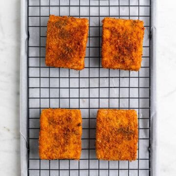 Cooked tofu pieces on a wire rack on a lined baking sheet.
