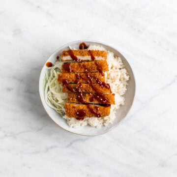 Bowl of tofu katsu served over rice with cabbage on the side and sesame seeds on top.