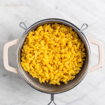 Cooked pasta draining in a colander over a pot.