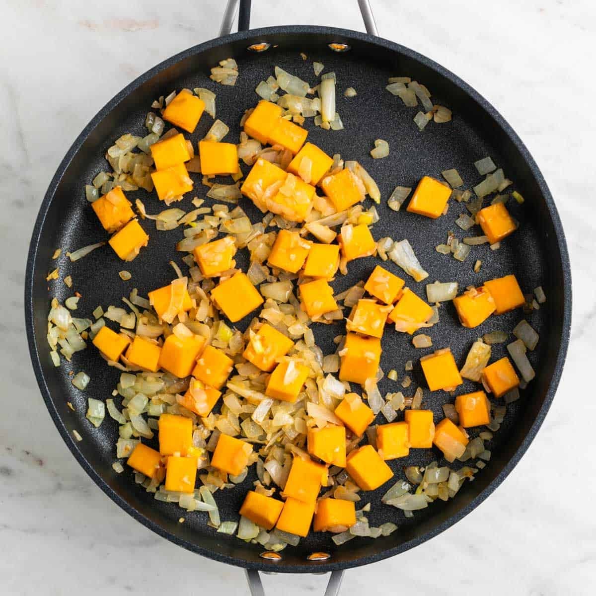 Sautéed onion, garlic, and butternut squash in a skillet.