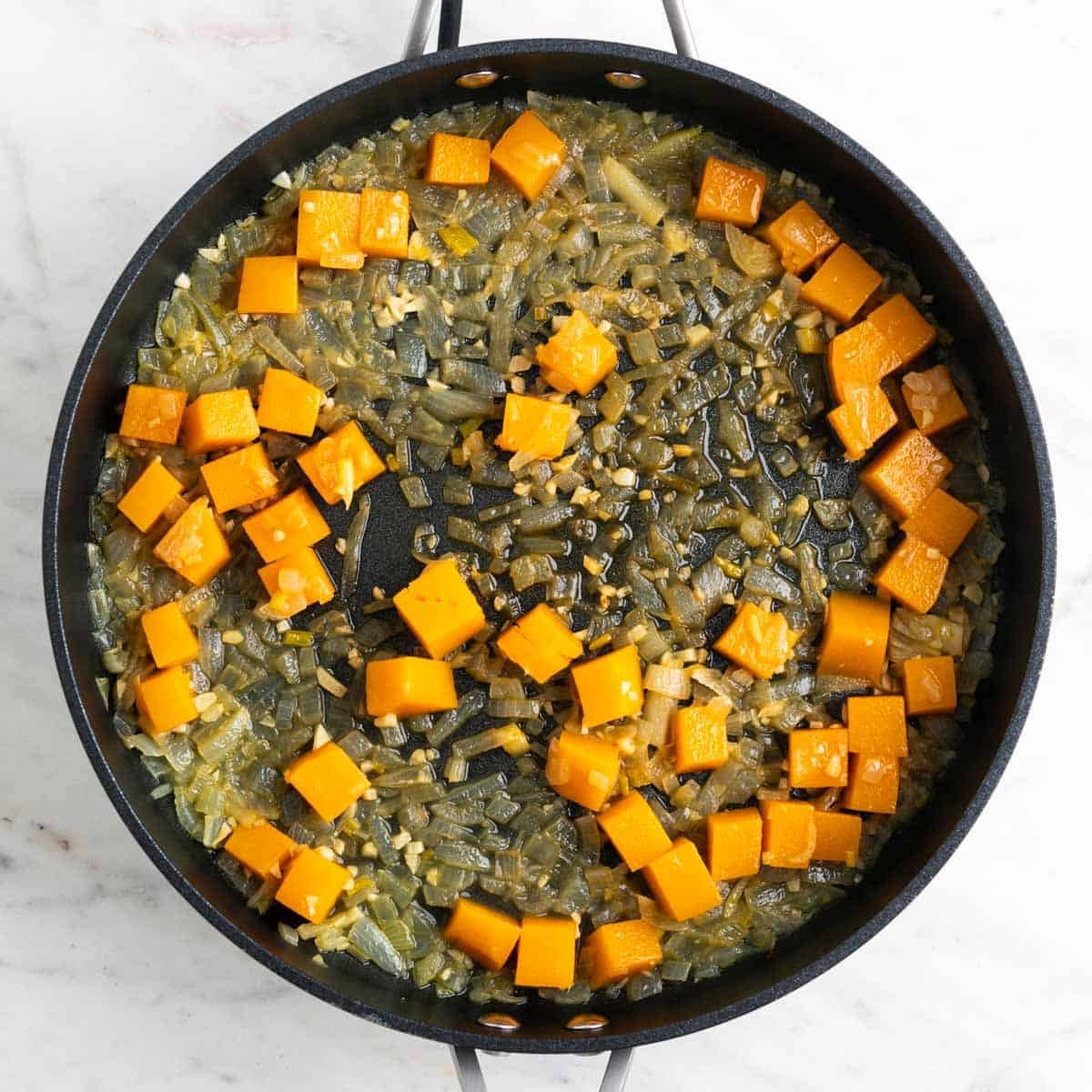 Skillet with onion, garlic, and butternut squash reduced in vegetable broth.