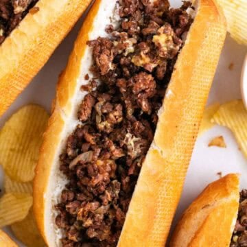 Vegan Philly cheesesteak sandwiches with chips on the side.