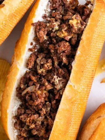 Vegan Philly cheesesteak sandwiches with chips on the side.