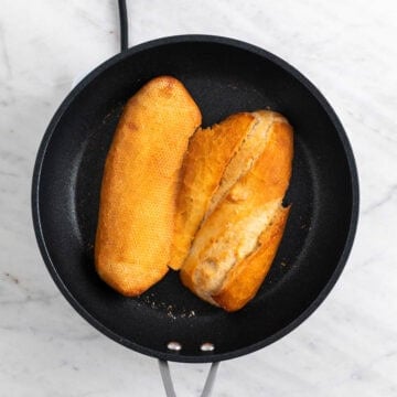 Sandwich roll toasting in a skillet.