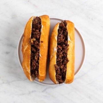 Two Vegan Philly cheesesteak sandwiches on a plate.