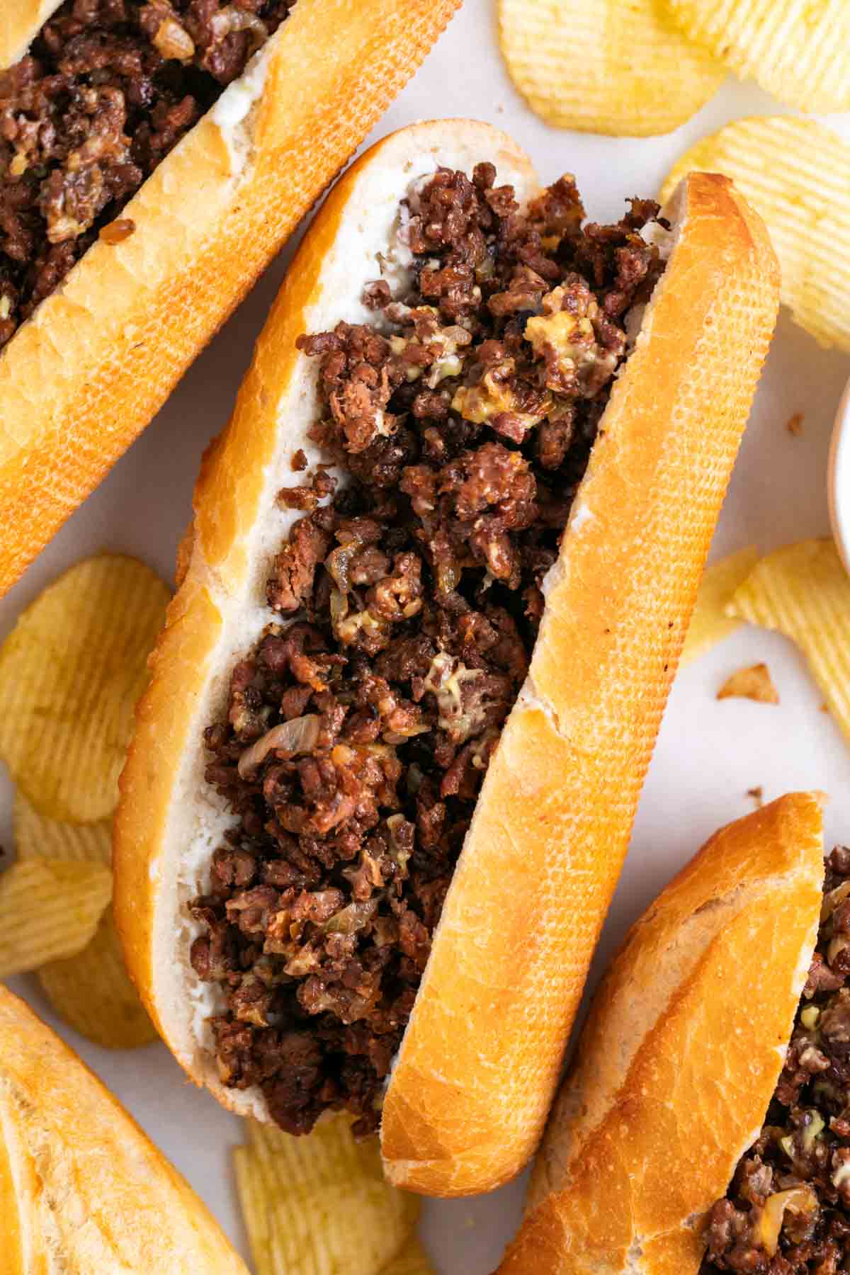 Vegan Philly cheesesteak sandwiches served with chips.