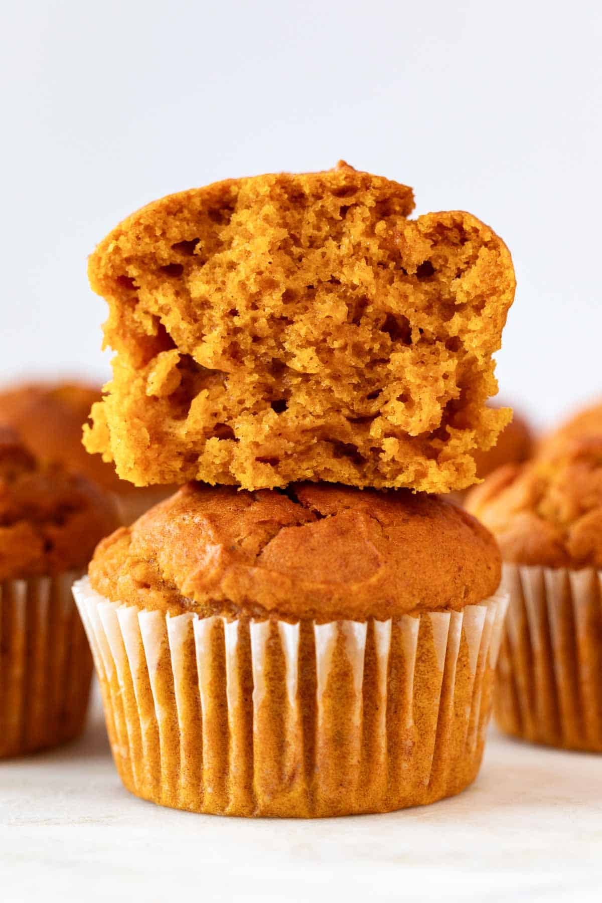 Stacked vegan pumpkin muffins with one sliced on top.
