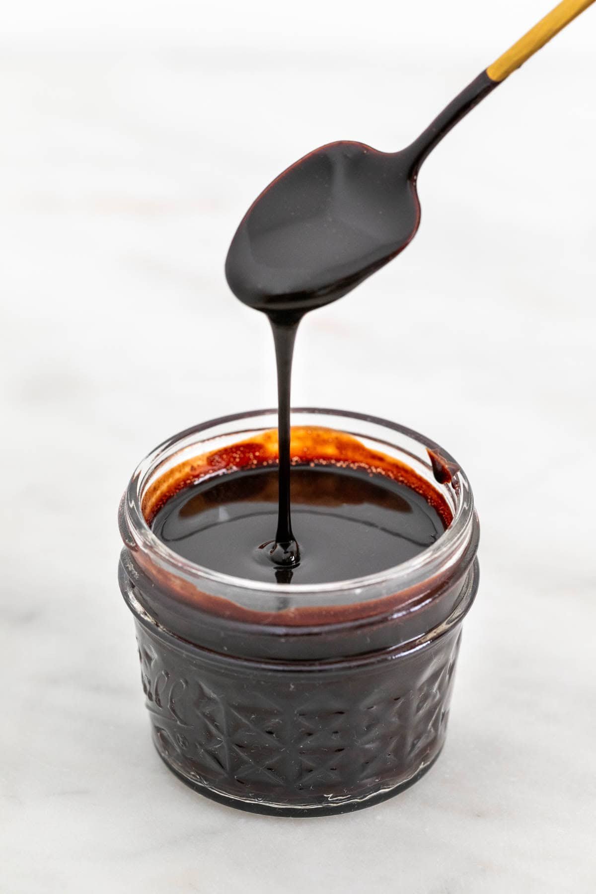 Jar with vegan chocolate sauce and a spoon pouring the sauce.