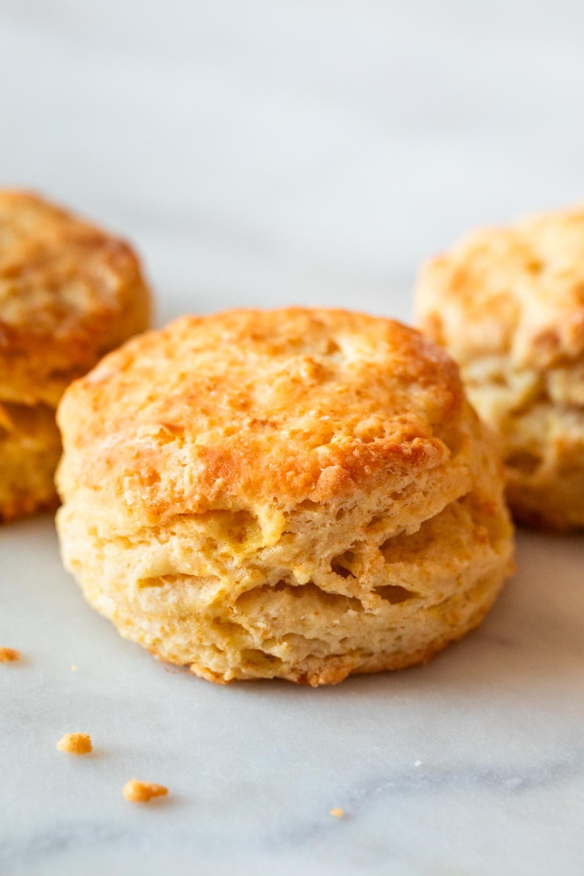Flaky vegan biscuit in foreground, with two biscuits blurred in background.