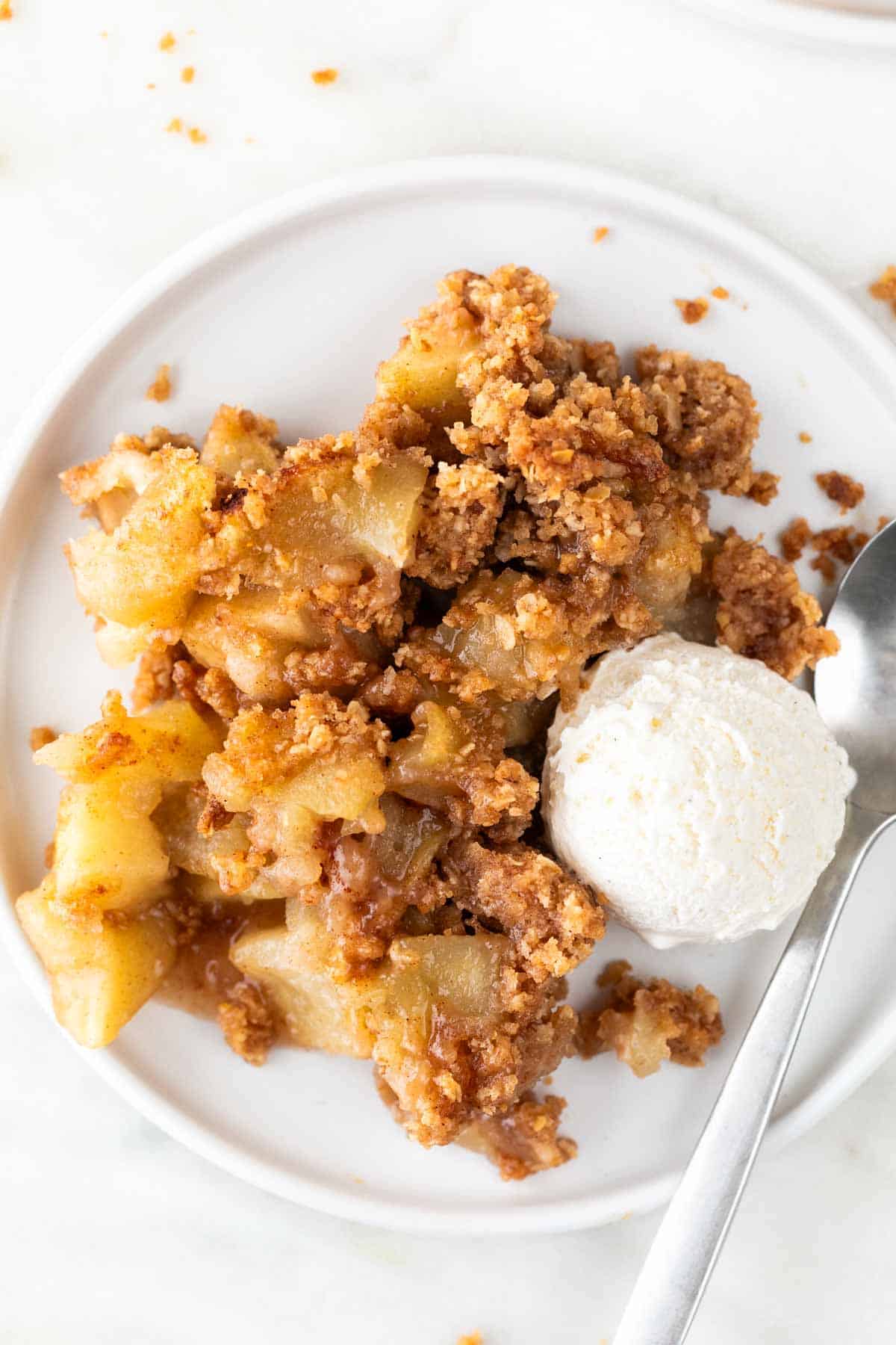 Serving of vegan apple crisp topped with vegan vanilla ice cream and a spoon.