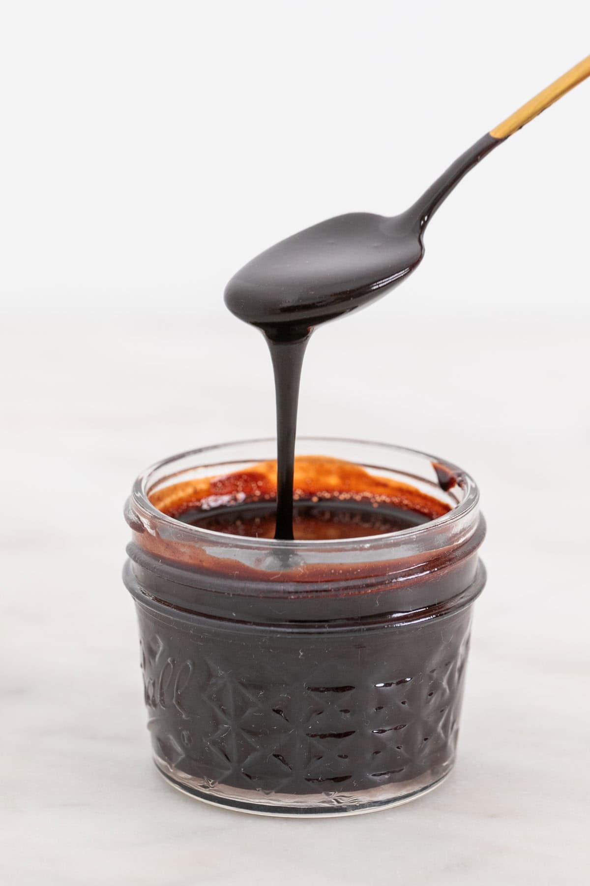 Spoon pouring vegan chocolate sauce into a glass jar.