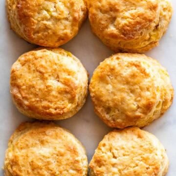 Six flaky golden biscuits arranged on a white marble background.