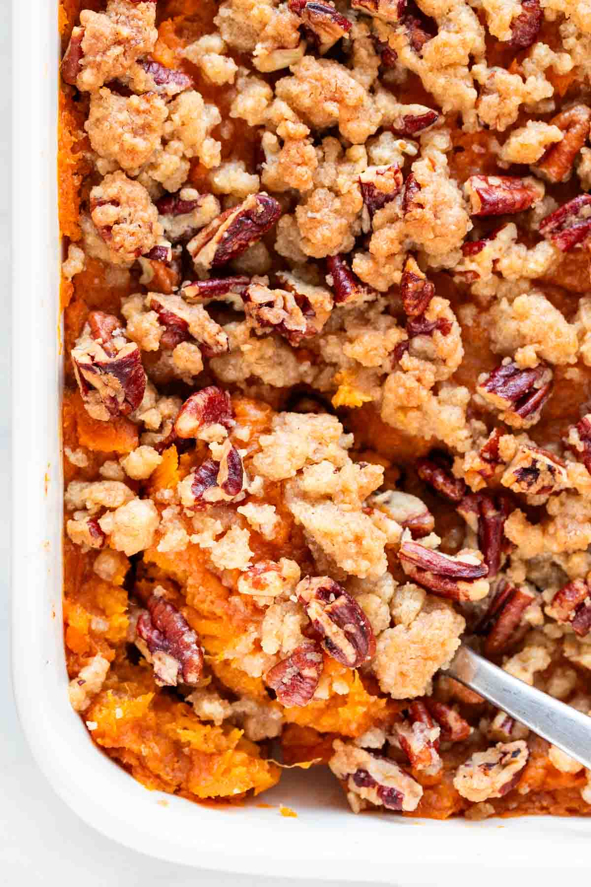 A baking dish of vegan sweet potato casserole with a spoon inside.