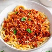 Bowl of tofu bolognese pasta topped with fresh basil and vegan Parmesan.