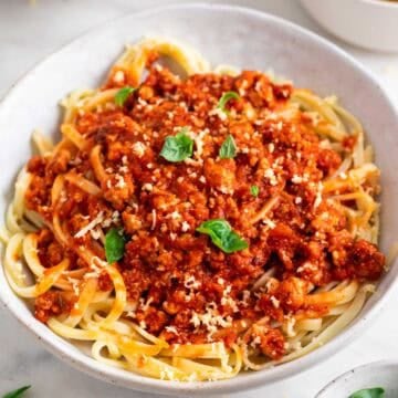 Bowl of tofu bolognese pasta topped with fresh basil and vegan Parmesan.