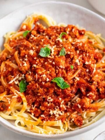 Bowl of tofu bolognese pasta topped with fresh basil and vegan Parmesan.