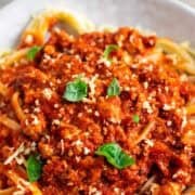 Bowl of spaghetti with tofu bolognese, vegan Parmesan, and basil.