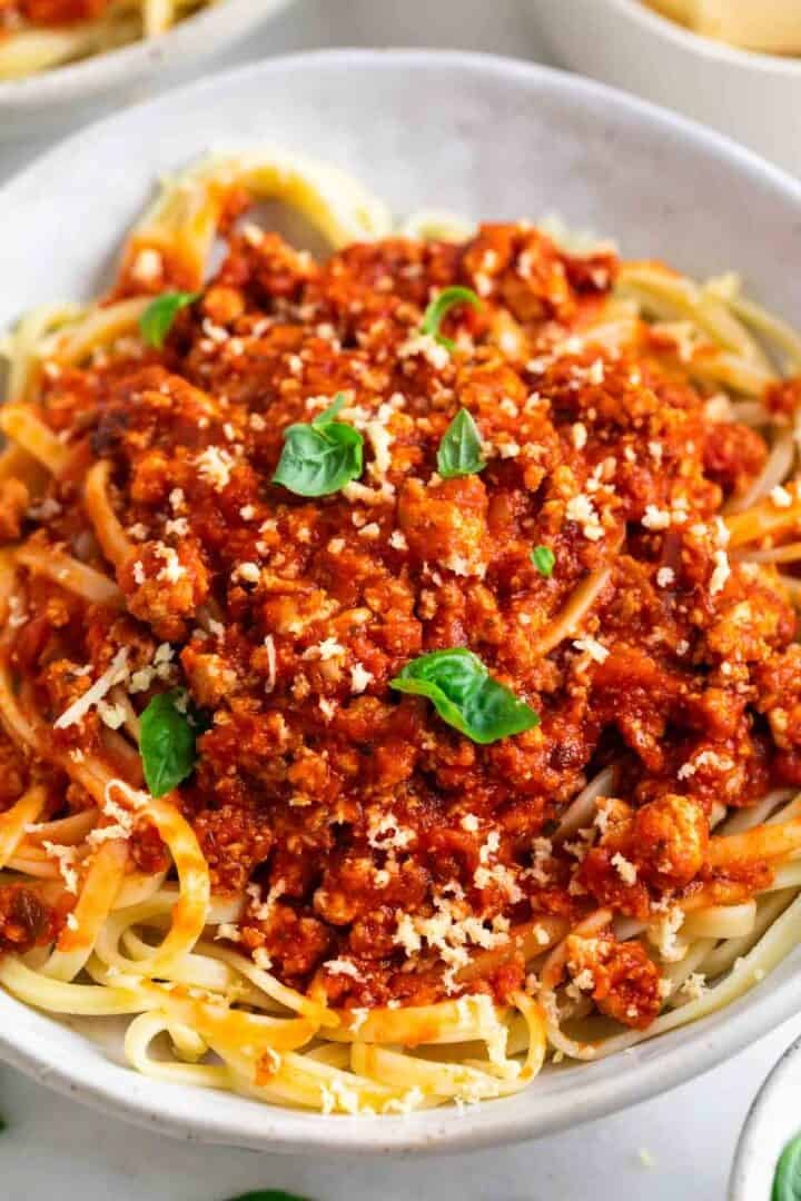 Tofu bolognese sauce over spaghetti in a bowl, topped with vegan Parmesan and fresh basil.