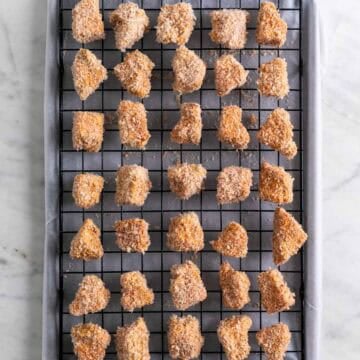 Breaded tofu nuggets on a wire rack on a lined baking sheet before cooking.