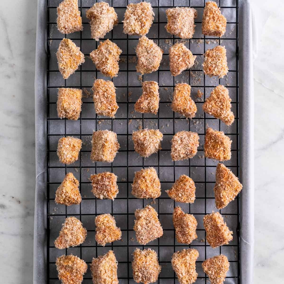 Breaded tofu nuggets on a wire rack on a lined baking sheet before cooking.