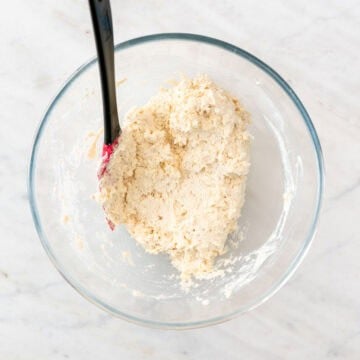 Shaggy vegan biscuit dough mixed gently in a bowl using a spatula.