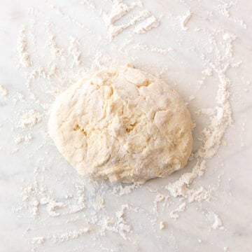Sticky vegan biscuit dough being gathered on a floured surface.