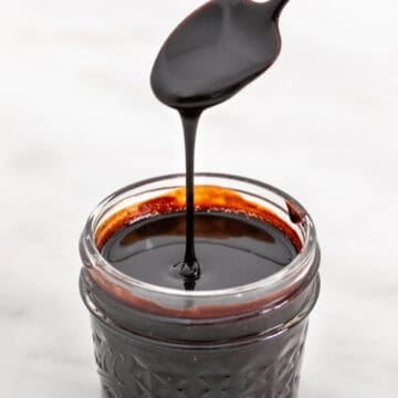 Homemade vegan chocolate sauce in a jar with a spoon pouring it.