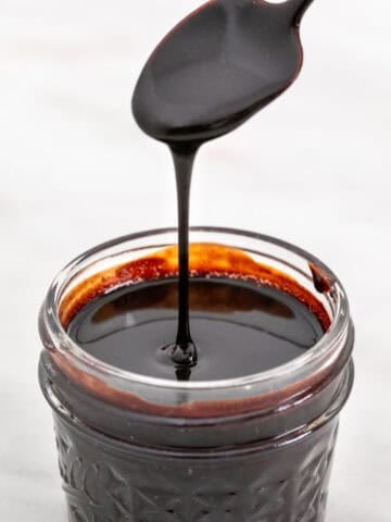 Homemade vegan chocolate sauce in a jar with a spoon pouring it.