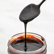 Vegan chocolate sauce being poured from a spoon into a jar.