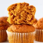 Stacked vegan pumpkin muffins with the top one sliced and more in the background.